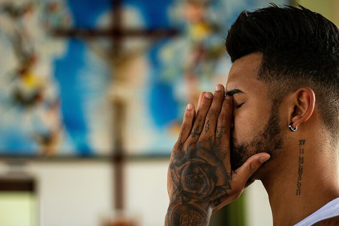 Man with tattoos praying in church setting, representing diversity in male-dominated fields.