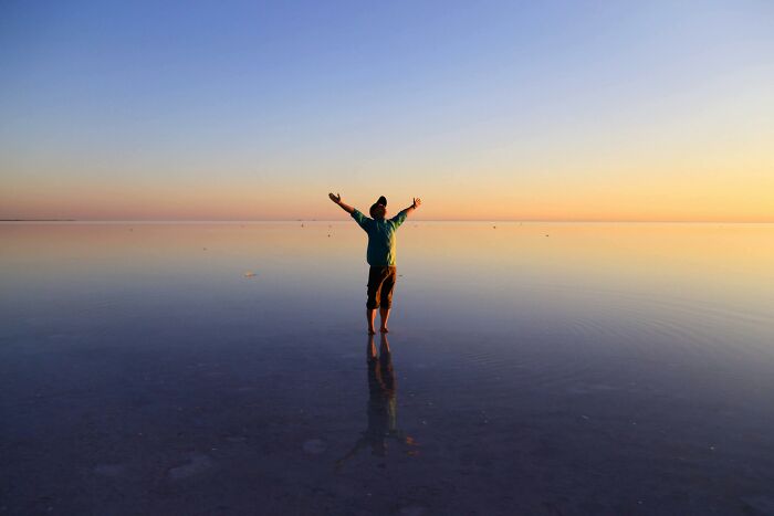 Person enjoying peace and quiet, standing with arms raised on a serene beach during sunset.