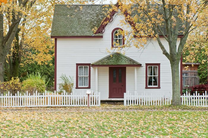 A quaint white house with a red door and autumn leaves, representing serene family life.