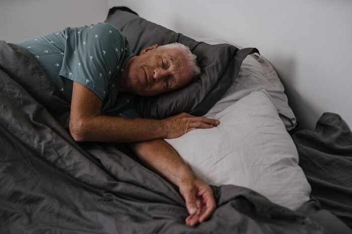 Elderly man sleeping peacefully in bed, highlighting relaxed posture in a serene setting.