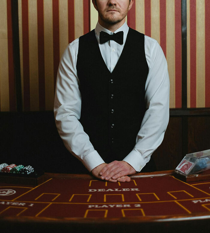 Casino employee in uniform standing at a poker table with chips and cards, illustrating behind-the-scenes moments.