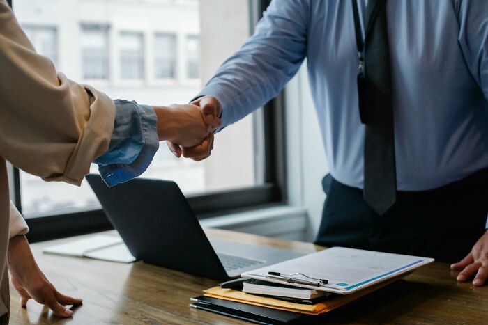 Two people shaking hands over a desk with documents and a laptop, signifying influential moments in history.