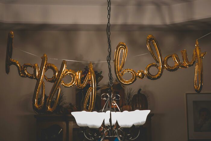 Golden birthday balloons spelling "happy bday" hang in a quiet, dimly lit room.