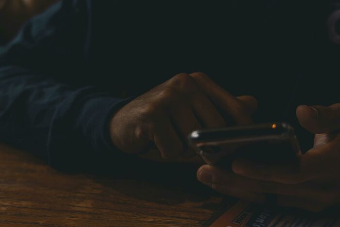 A person in dim lighting, focused on a smartphone, symbolizing connection lost between former best friends.