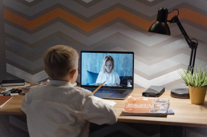 Child in virtual class, learning secrets about jobs, at a wooden desk with a lamp and magazines.