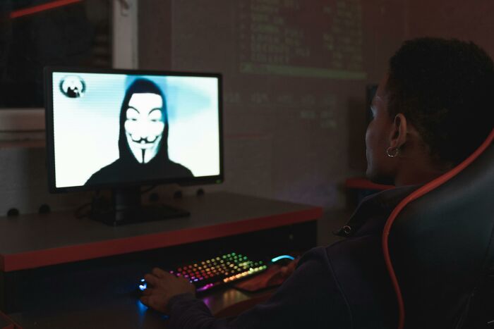 Person at computer, watching a hacker in a Guy Fawkes mask on the screen, symbolizing influential historical moments.