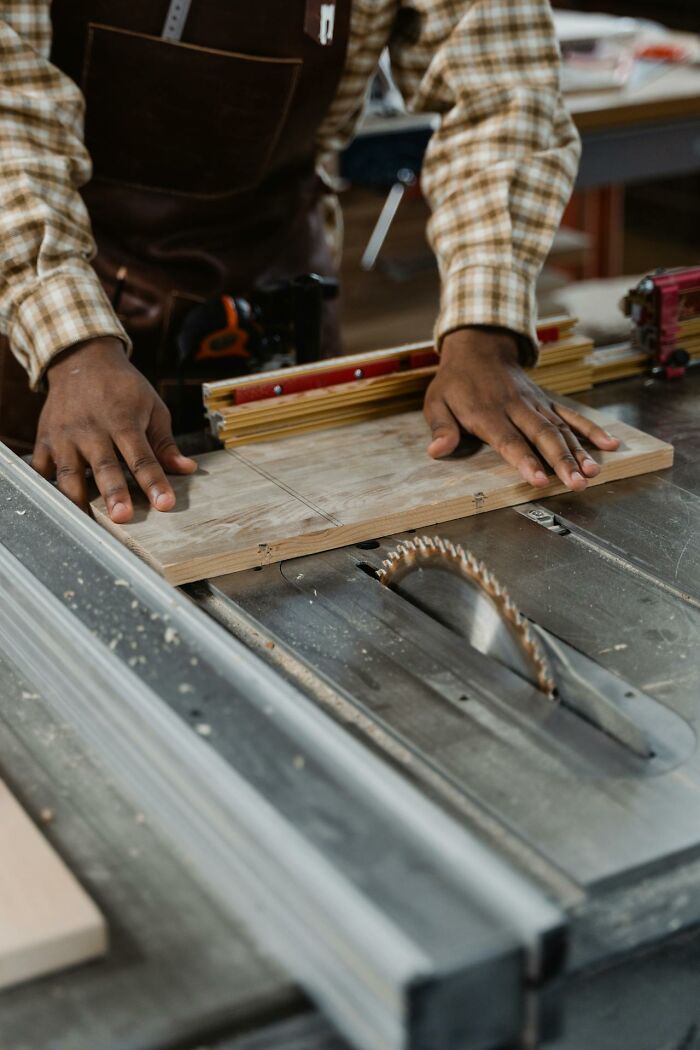 Person in plaid shirt using a table saw in a workshop, illustrating a DIY project for "moment realized dating idiot" context.