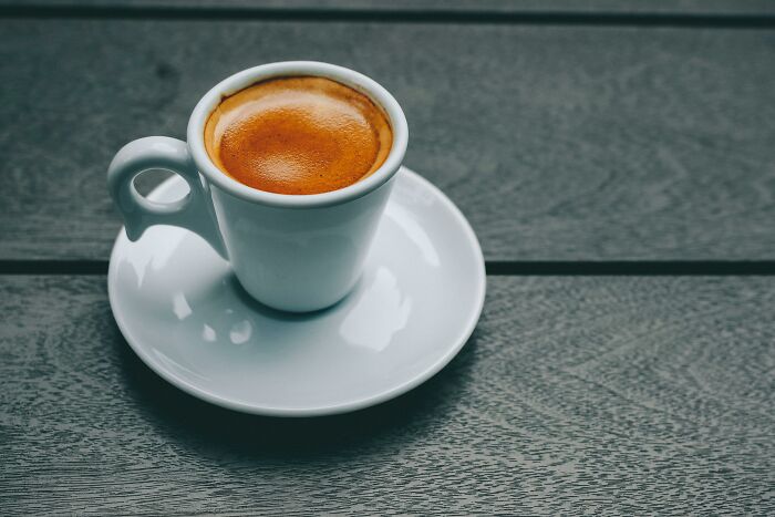 Espresso in a small white cup on a dark wooden table, highlighting the "WomenInMaleFields" trend theme.