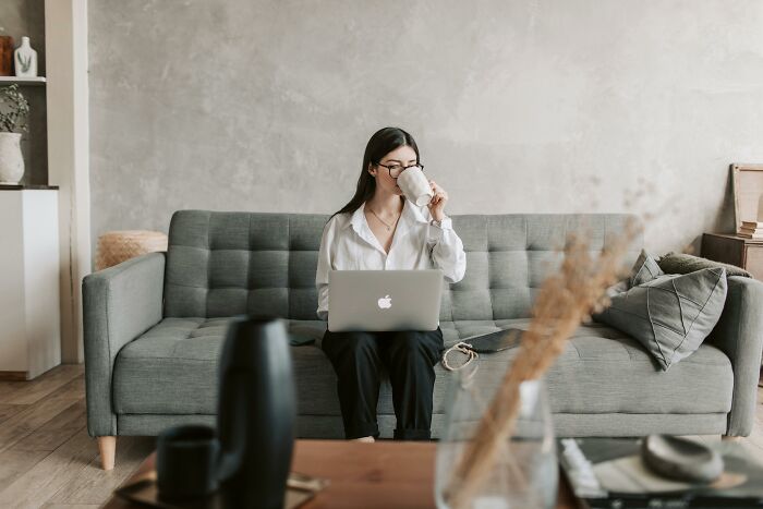 Person enjoying peace and quiet while working on a laptop from a cozy couch, sipping coffee.