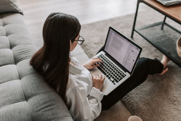 Woman in glasses using a laptop while sitting on the floor, demonstrating the importance of exercise in daily routine.