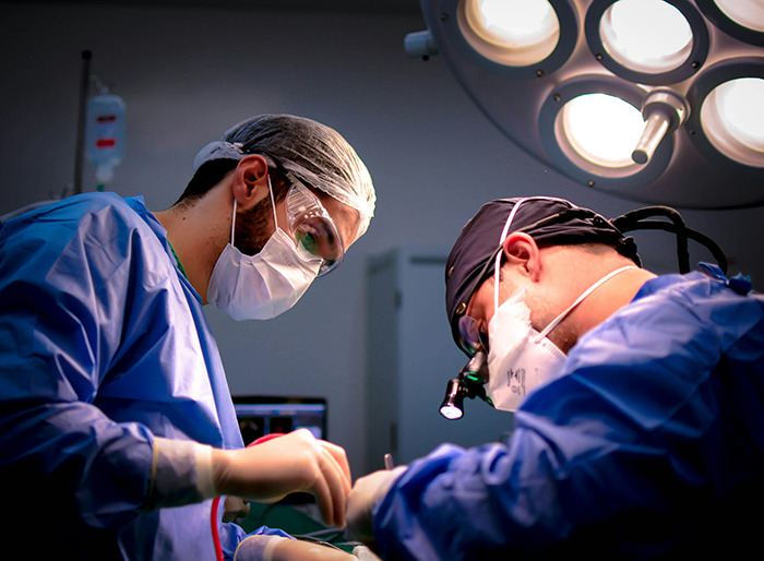 Surgeons in operating room, wearing masks and scrubs under bright surgical lights.