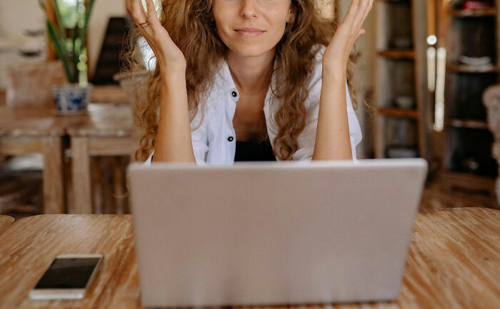 Woman at desk with laptop, hands raised, realizing dating an idiot.