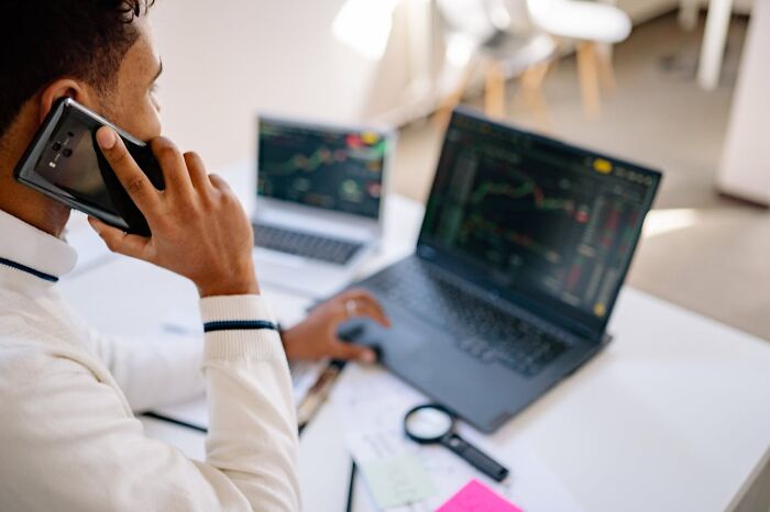 Person at desk with laptop and phone, analyzing stock charts, representing 'fun' jobs that may not be as enjoyable as they seem.