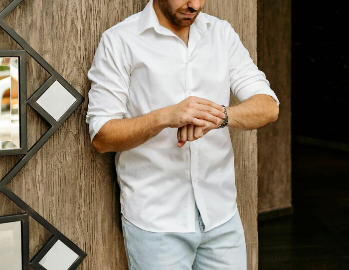 Man in white shirt checking watch, standing against textured wall, highlighting moment realized dating an idiot.