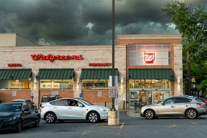 Walgreens storefront with cars parked outside under a cloudy sky.