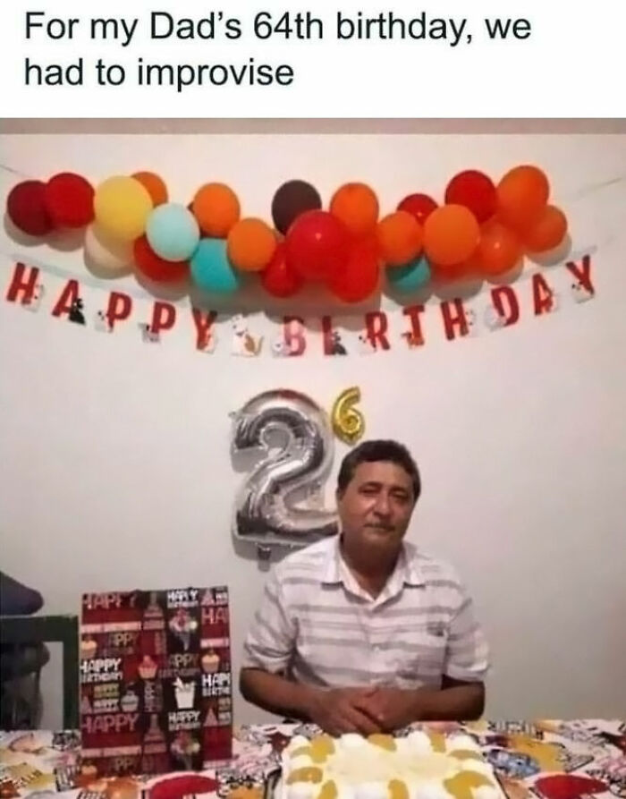 Man at birthday party with improvised "64" sign using balloons, surrounded by colorful decorations and cake.