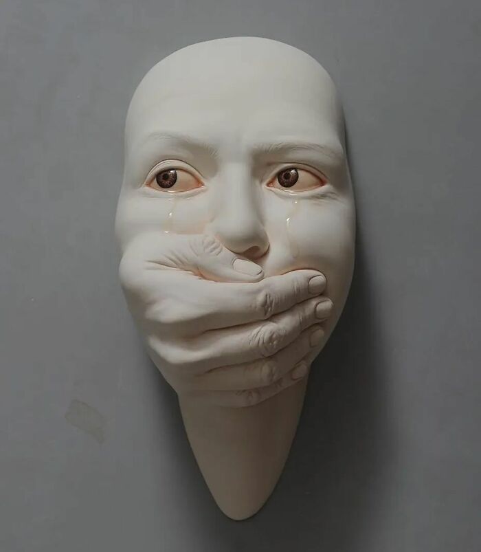 Surrealism and realism blend in this expressive sculpture of a face with a hand covering the mouth, evoking deep emotion.