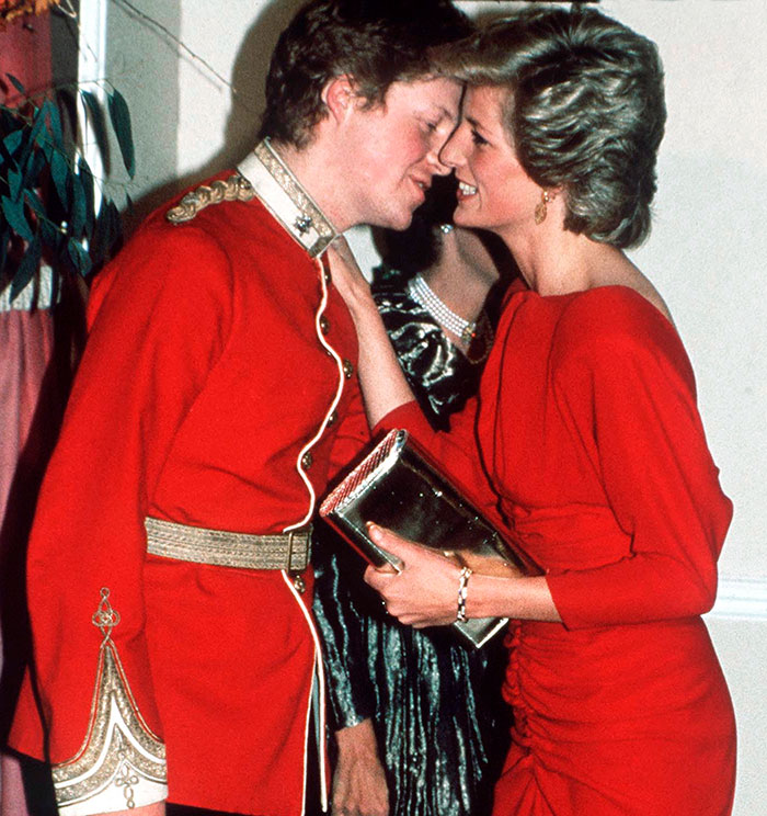 A man in a red uniform interacts closely with a woman in a red dress at a formal event.