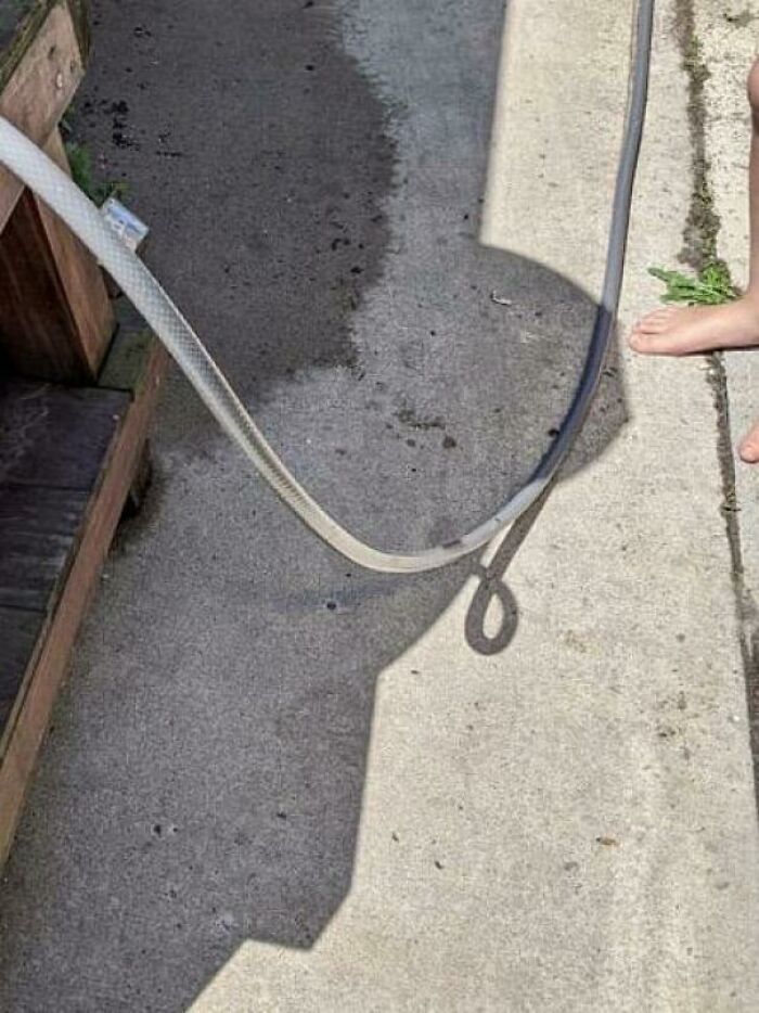 A hose creates an optical illusion, resembling bad renders, with shadows on a concrete surface.