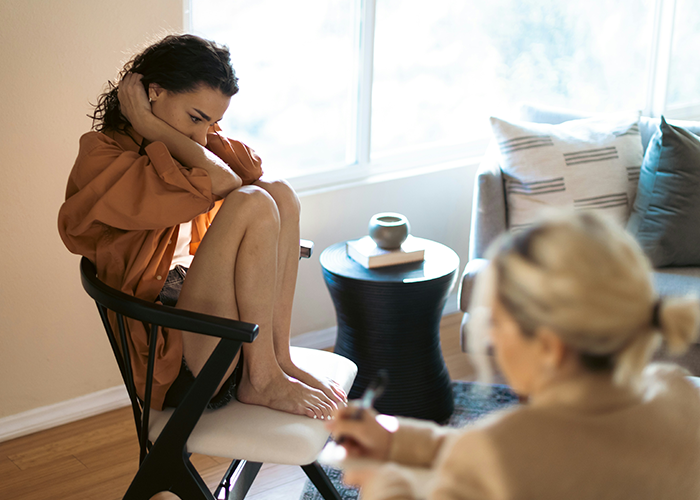 Woman upset after being uninvited from baby shower, sitting on chair indoors.