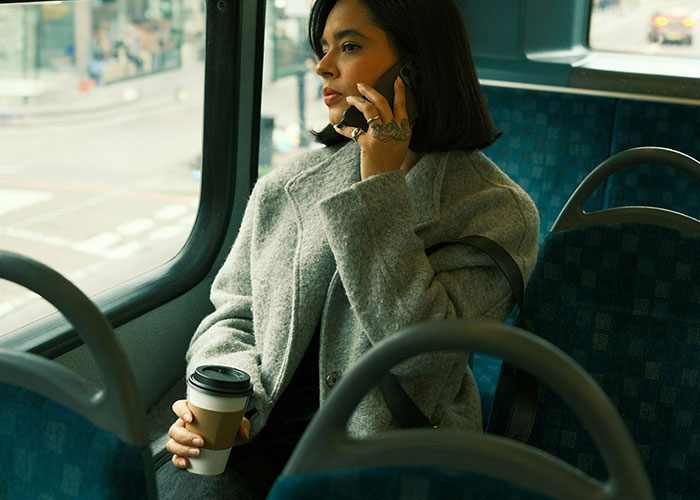 Woman on a bus, holding a coffee, talking on the phone, after being uninvited from a baby shower.