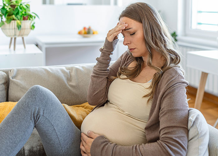 Pregnant woman looking stressed on couch, hand on forehead, related to baby shower food delivery conflict.