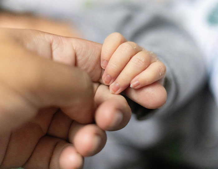 Toddler's hand gently holding an adult's finger, conveying tenderness and care amidst a family concern.