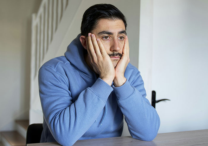 Man in blue hoodie looking concerned about awkward living situation.