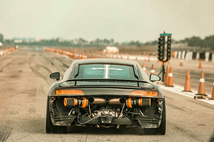 Retiree's gift: a custom sports car on a racetrack, showcasing rear modifications under a cloudy sky.