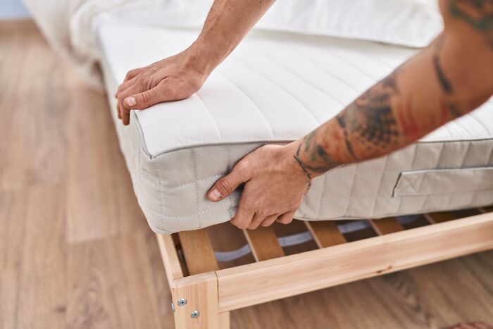 Hands adjusting a mattress on a wooden bed frame, illustrating gifts retirees buy for comfort.