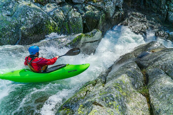 Retiree kayaking through rapids in a bright green kayak, enjoying a retirement gift to himself.