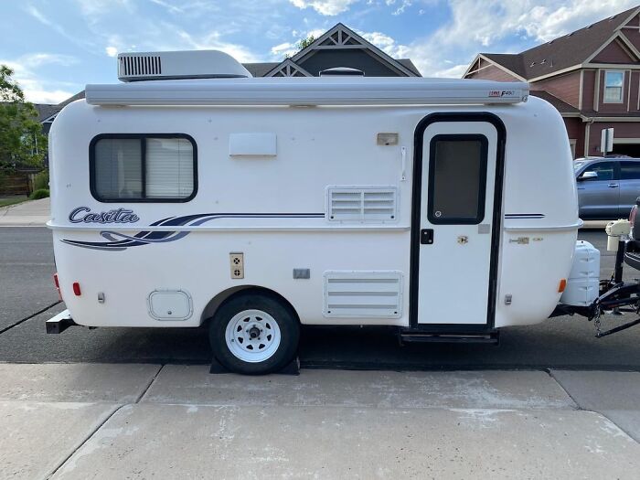 Small white camper trailer parked on suburban street, ideal gift for retirees seeking travel adventures.