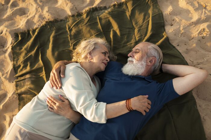 Retirees relaxing on a blanket at the beach, embracing and enjoying their time together.