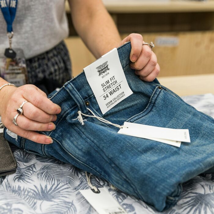 Traveler holding jeans with a size tag, reflecting cringeworthy shopping mishap.