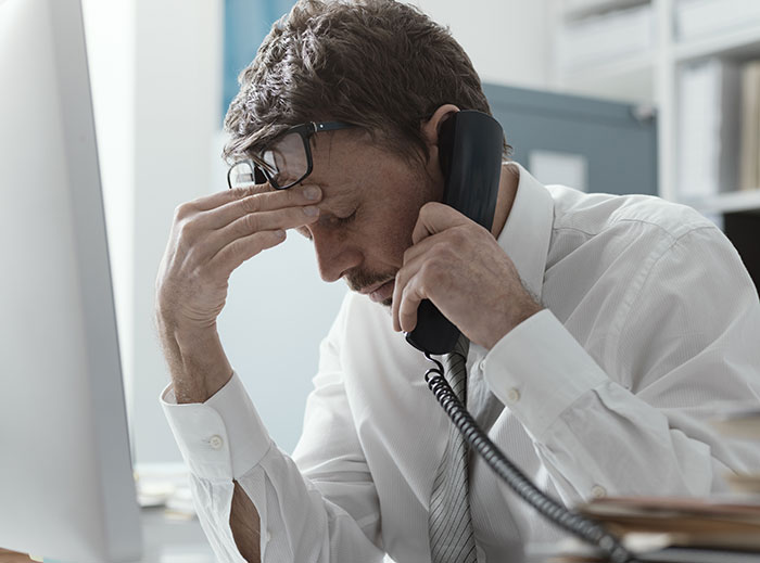 Man in office holding phone, looking stressed about denied insurance claims.