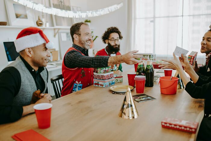 People exchanging Secret Santa gifts at a holiday gathering, with festive decorations and beverages on the table.