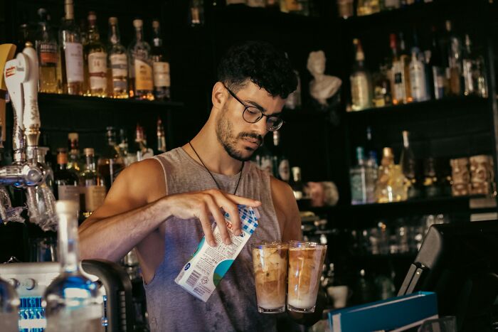 Barista pours milk into iced coffee drinks while working at a busy bar, highlighting the reality of 'fun' jobs.