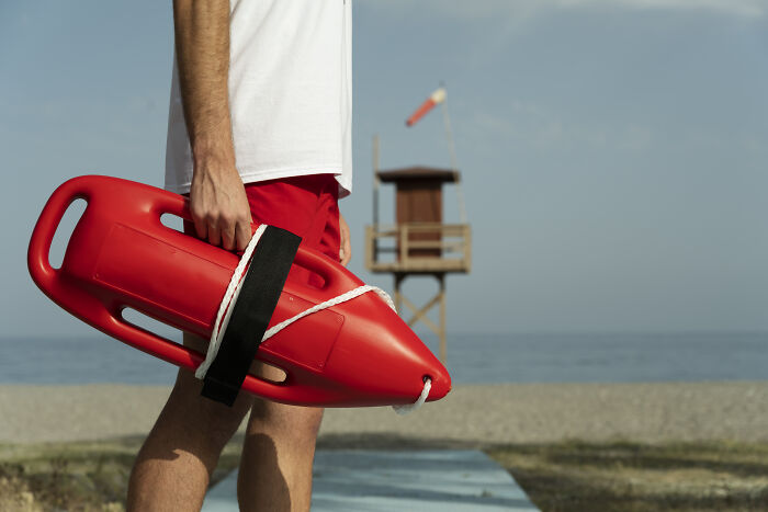 Person holding a red buoy on the beach, illustrating a challenging job experience.