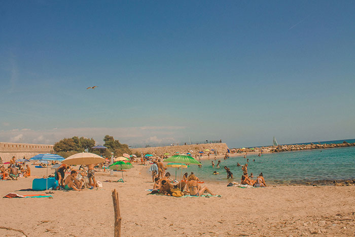 People enjoying a sunny day at the beach, with colorful umbrellas and the sea in the background.