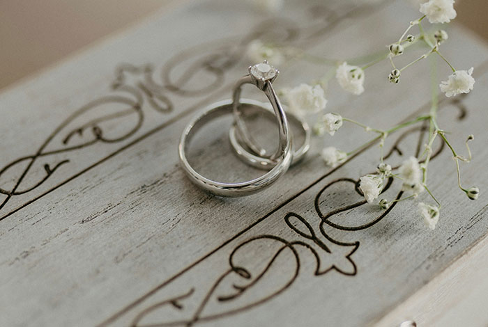 Wedding rings on an engraved wooden surface, symbolizing marriage challenges and potential failure, adorned with delicate flowers.