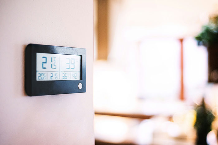 Digital thermostat on a white wall showing temperature and humidity, illustrating signs of marriage issues.