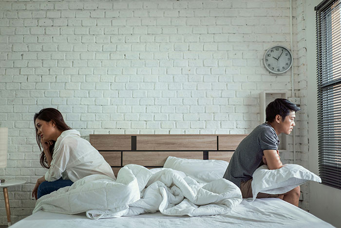 Couple sitting back-to-back on bed, indicating marriage destined to fail, in a tense bedroom atmosphere.