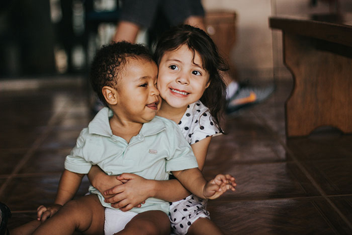 Two young children sitting on the floor, playing and smiling joyfully, capturing moments of happiness and innocence.