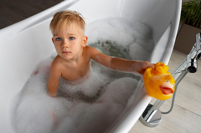 Child in a bathtub holding a rubber duck, illustrating neglect as a sign of terrible parents.