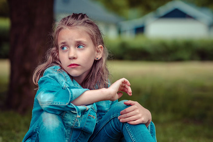 A worried girl in a park wearing a denim jacket, representing signs of distress possibly due to terrible parenting.