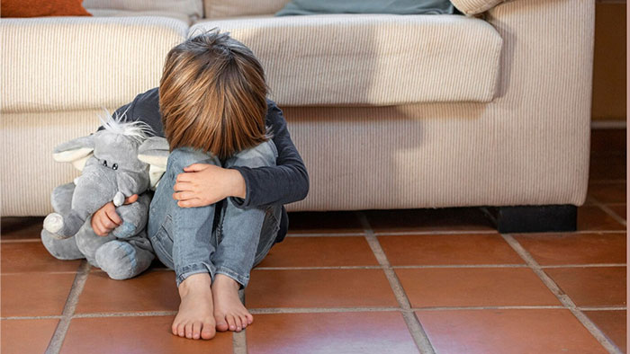 Child hugging knees on the floor, holding a stuffed elephant, highlighting signs of terrible parents.