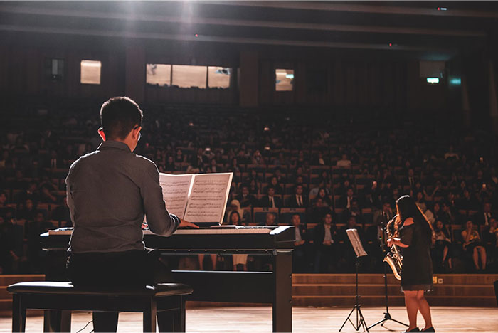 A pianist and saxophonist performing on stage in front of a large audience, highlighting musicianship.