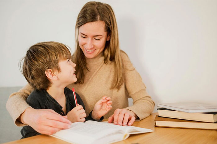 Parent reading with a child at a table, surrounded by books, demonstrating signs of positive parenting.