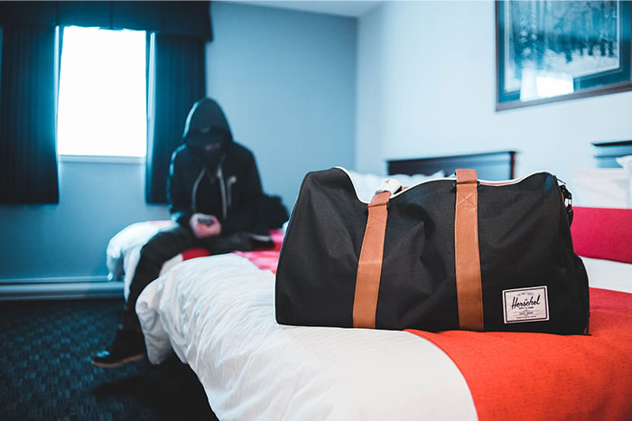 Person in a dark room sitting on a bed with a large duffel bag in the foreground, highlighting signs of terrible parents.