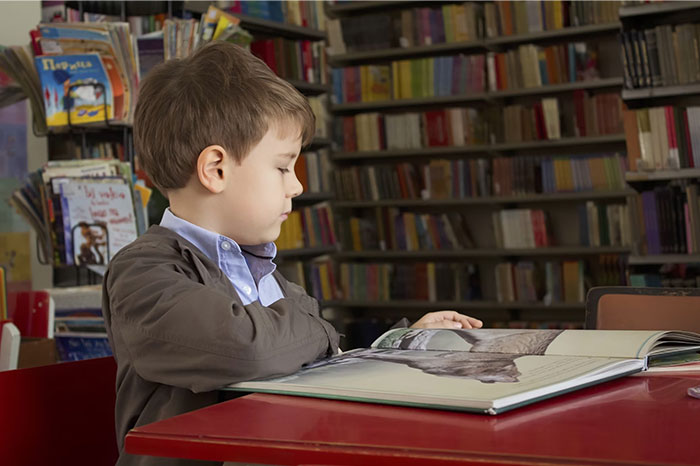 Child reading a book in a library, possibly seeking comfort from signs of terrible parents.